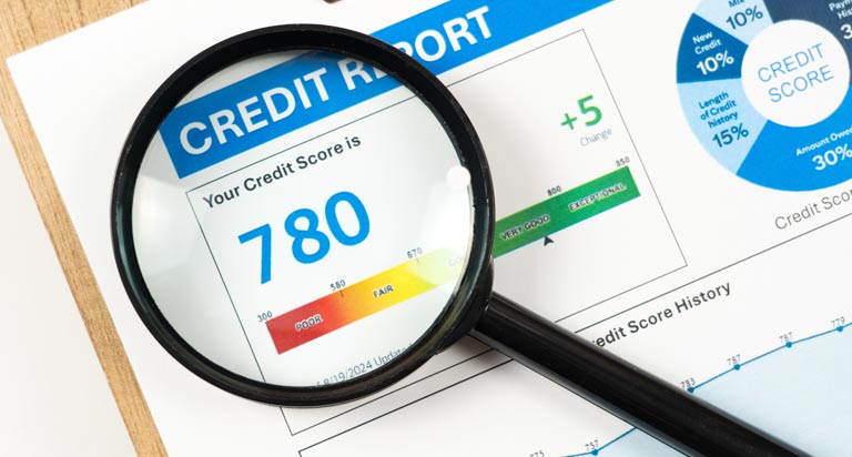 A credit report clipped onto a clipboard with a magnifying glass laying over the score portion, showing the score “780”.