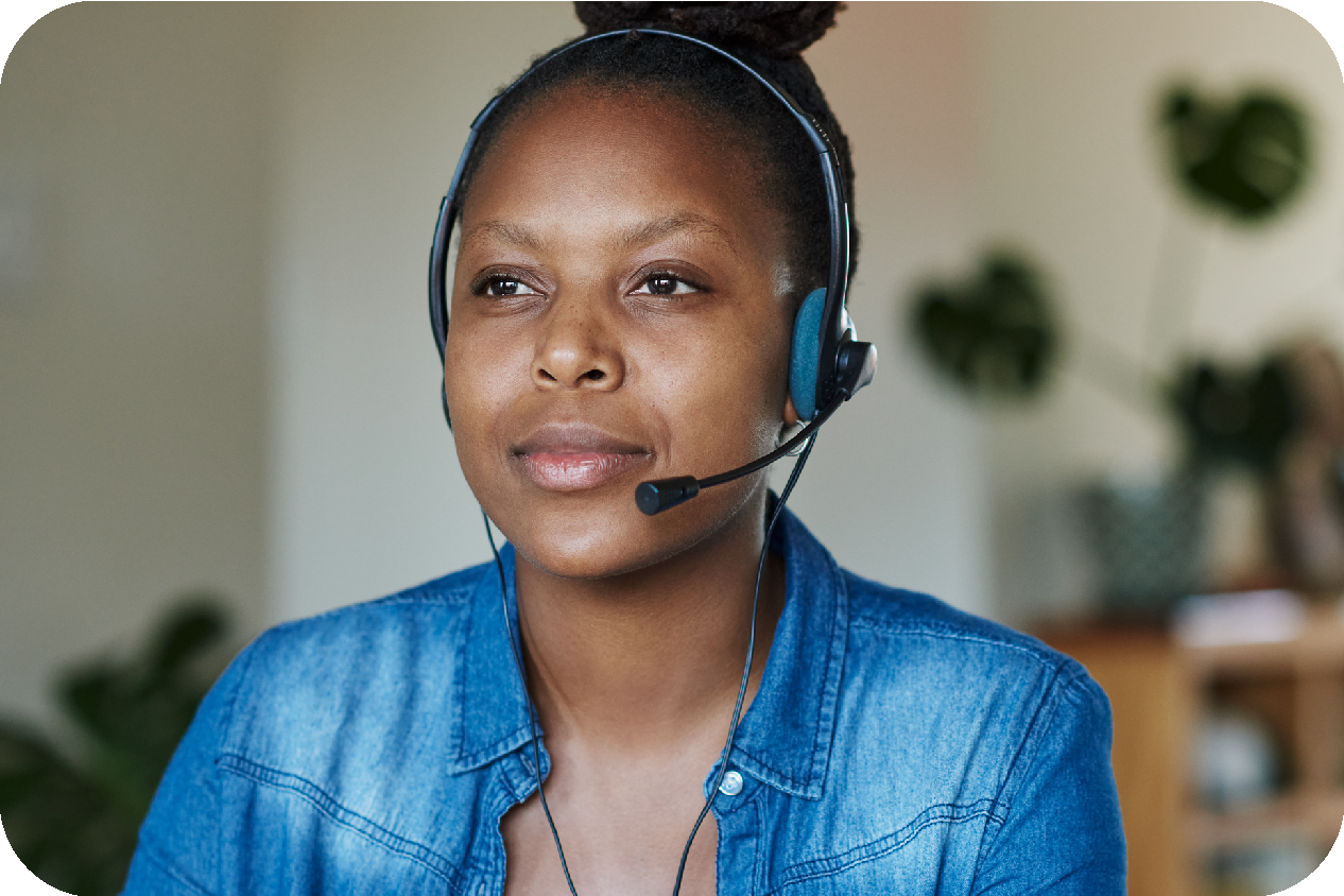 A scarved, customer support representative wearing a headset is smiling while talking with a customer.
