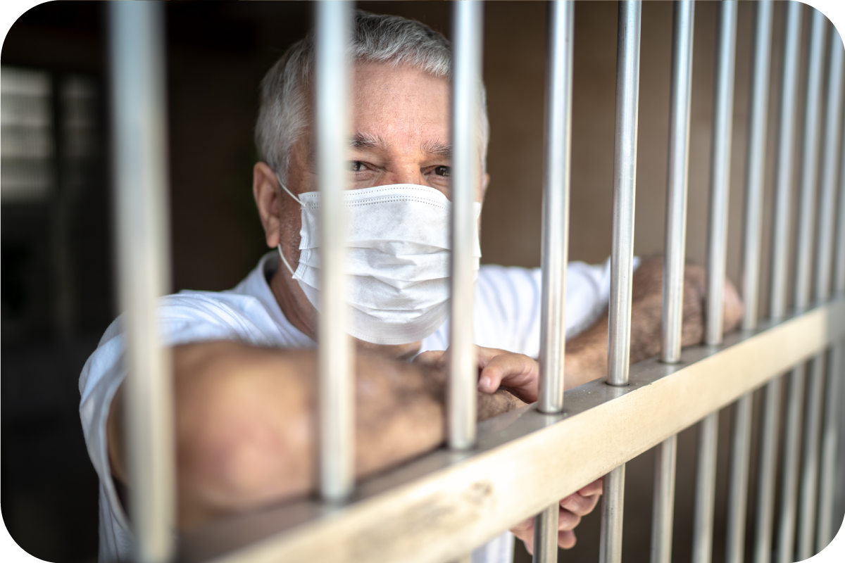 A man in a prison cell leaning on the bars looking directly into the camera