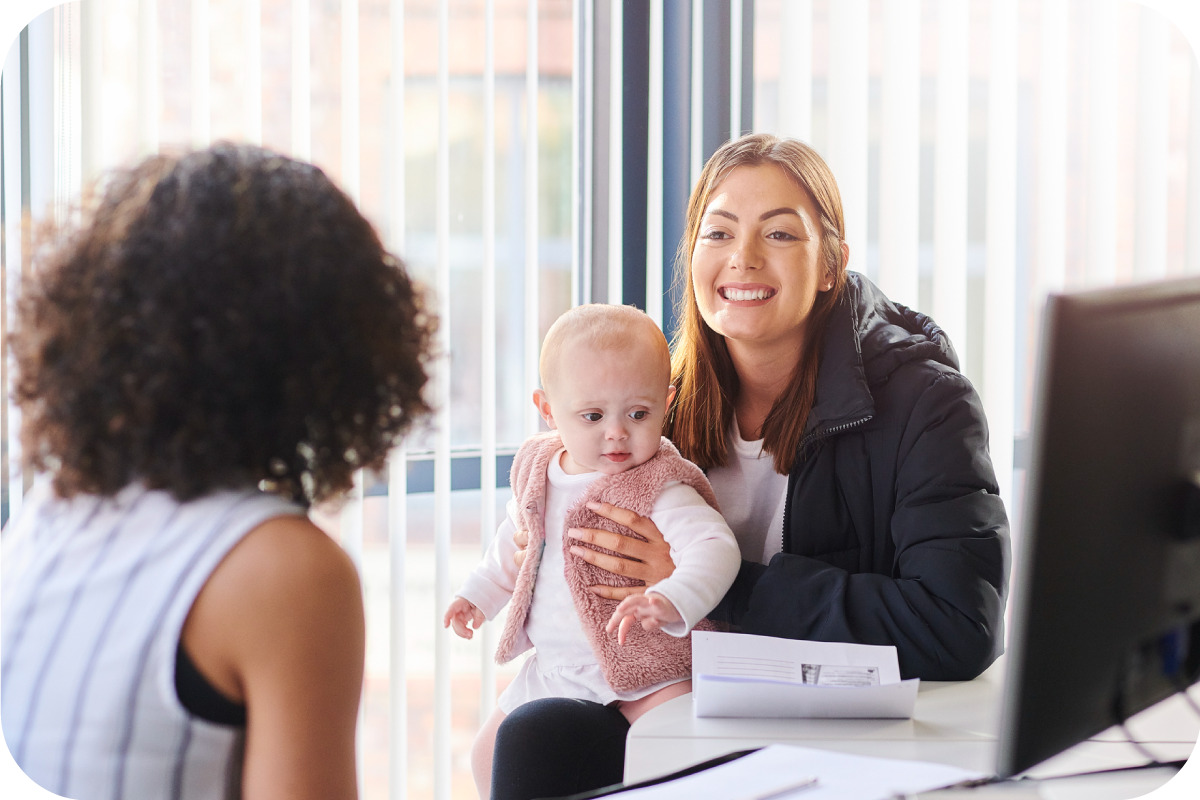 A young mother holding her baby while talking to a lady in an office