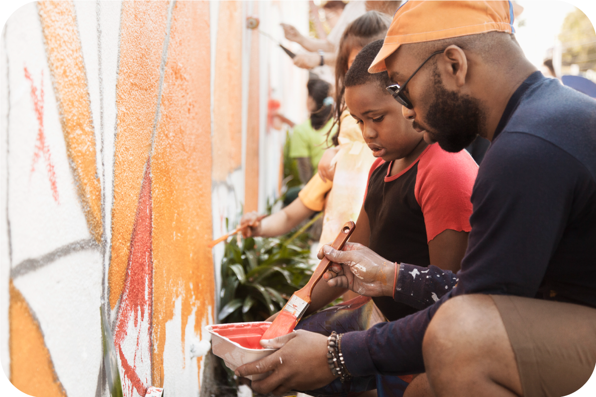 Man is helping child paint the exterior of a building