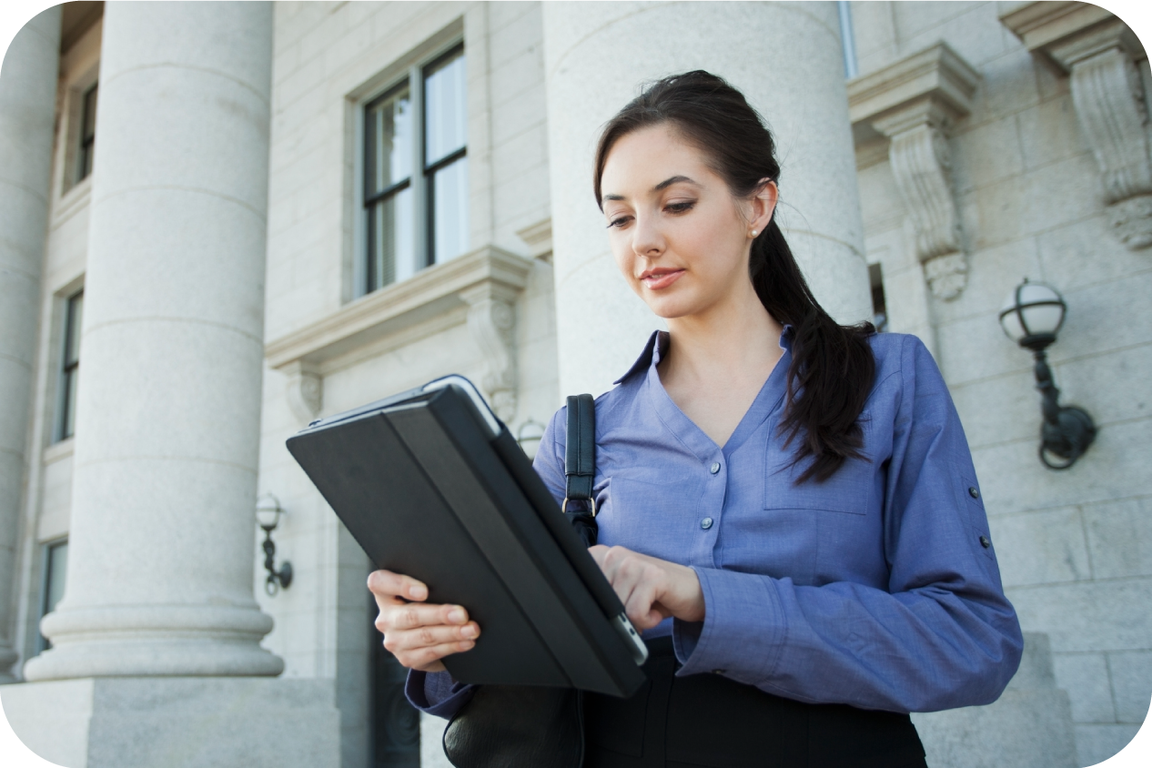 A young female paralegal or lawyer is using a tablet on the steps of a government building.