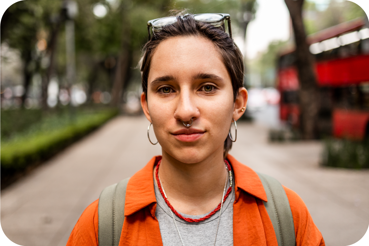 A young, non-binary person with a septum piercing is looking into the camera.