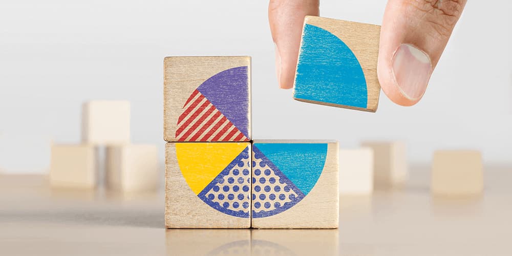 Four wooden blocks being stacked into a square with their faces aligning to create a pie chart with more wooden blocks in the background