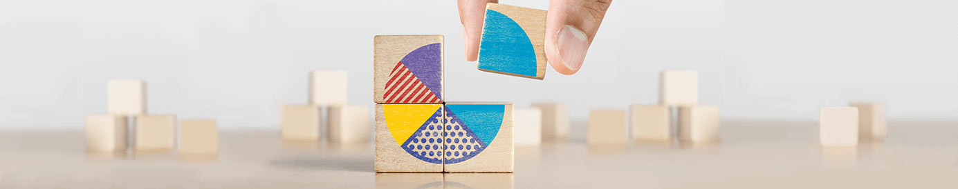 A person stacking four wooden blocks into a square with their faces aligning to create a pie chart with more wooden blocks in the background