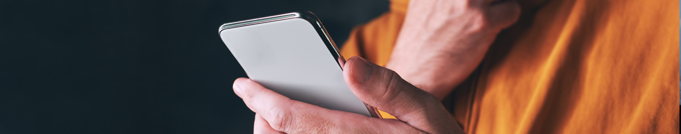 A man looks down at a phone he’s holding in one hand. He’s rubbing his bearded chin with the other hand.