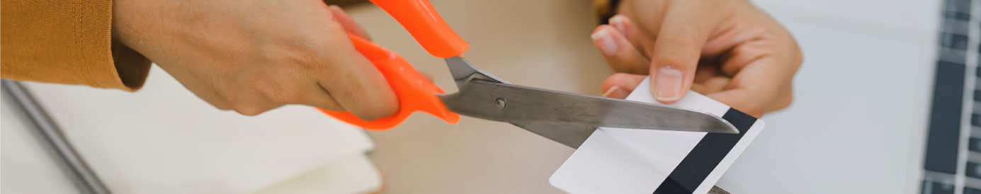 A woman's hands positioned over a desk as she cuts the credit card in her hand with scissors.