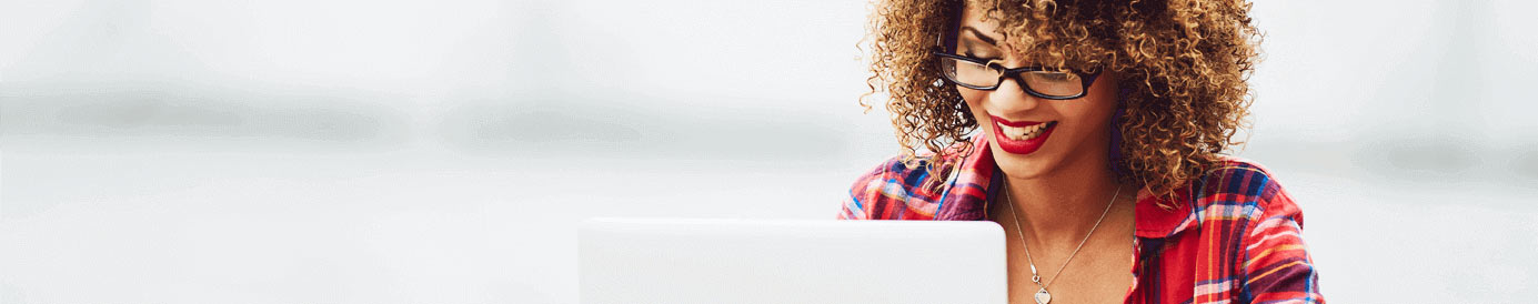 A woman wearing glasses and bright red lipstick smiling at her laptop screen