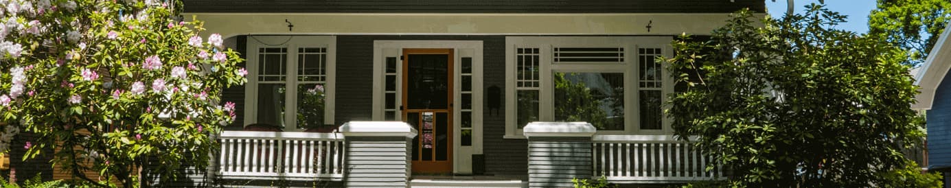 A house with a concrete walkway leading to stairs that go up to the front porch and that has a bush on either side of the house