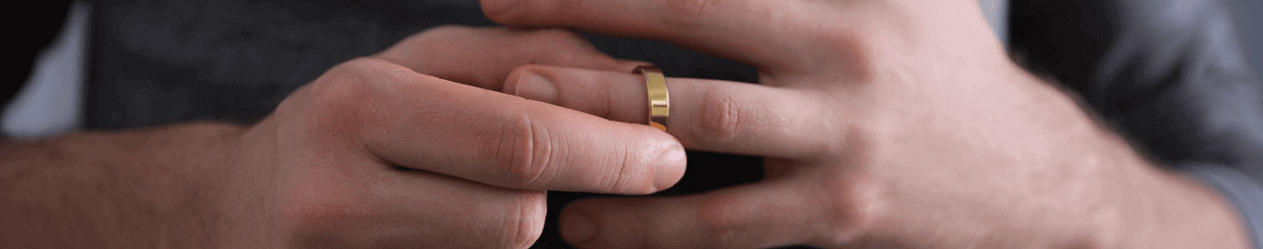 Mid-body crop of a man in a gray t-shirt removing his wedding ring.