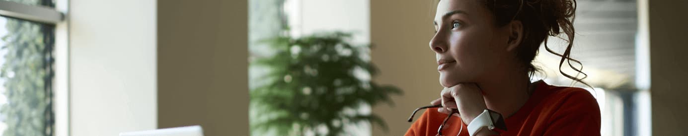 A woman rests her head on her left hand that is holding her glasses while she looks out a window