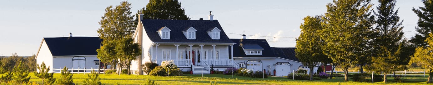 A large white farmhouse with a large three car garage and a white detatched shed behind it