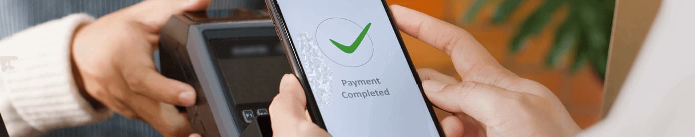 A person holding a payment terminal while another person holds their phone to the terminal as their phone shows Payment Completed