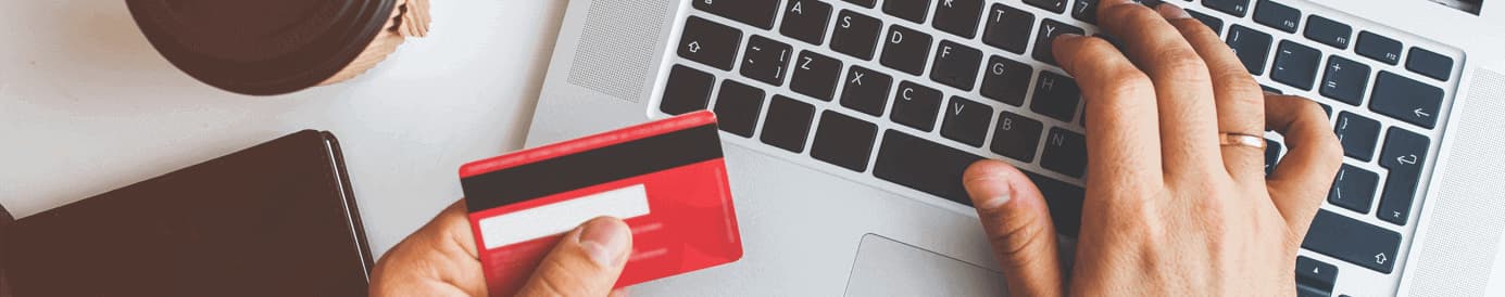 A person holding a red credit card in their left hand while typing on a laptop with their right hand