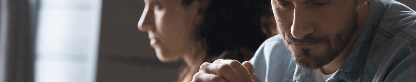 A man looking down while the woman in the background looks forward