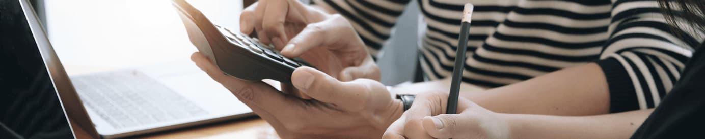 A person types on a calculator while someone else writes something with a pencil