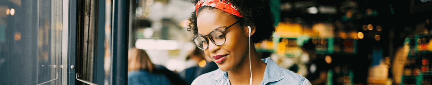 A woman wearing glasses and earbuds holding and looking at her laptop