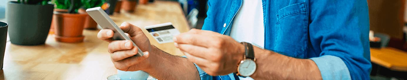 A person holding a credit card with their left hand and a cellphone with their right hand