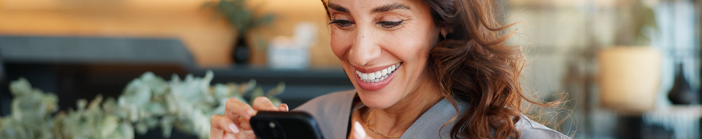 A business woman with dark red hair smiles brightly as she looks down at her phone and scrolls.