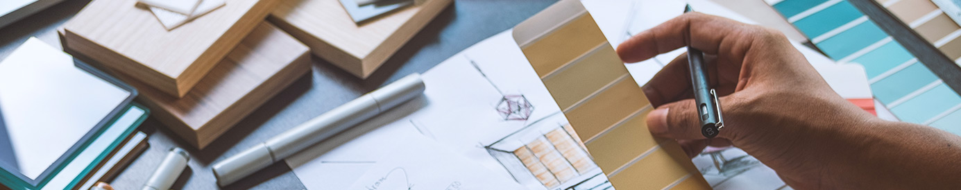 A desk with home improvement architectural designs and someone holding a pen looking over the plans.