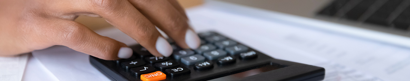 A person sits at a desk while using a calculator and laptop in front of them.