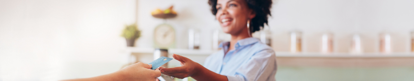 A smiling female cashier reaches over a counter to receive a debit card from a customer who is purchasing a green drink.