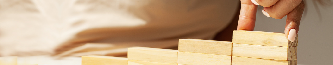 A woman stacks small rectangular wooden blocks in a row, placing them so they form stair steps.