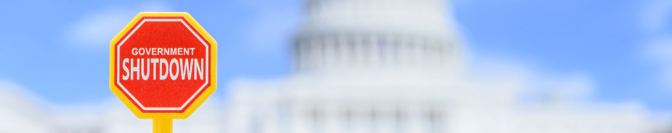 A blurred U.S. capitol building in the background with a red sign in the foreground that says 