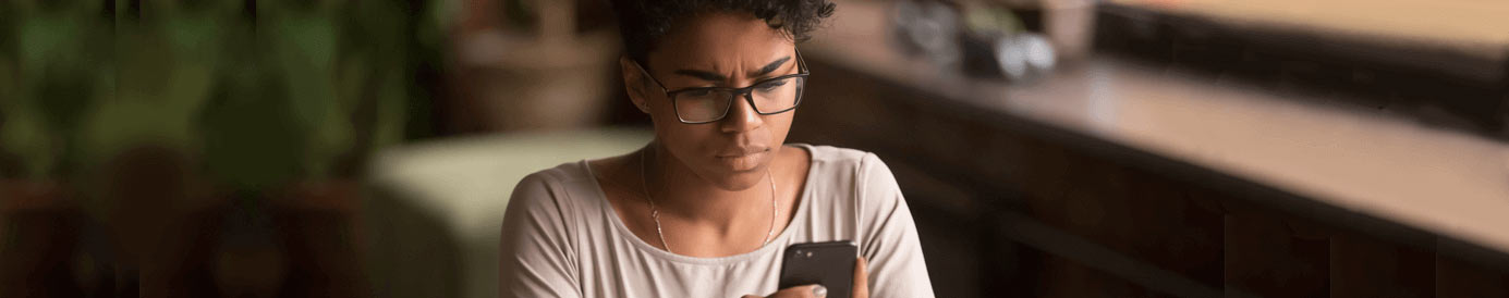 A woman wearing glasses stares intently at her cellphone screen