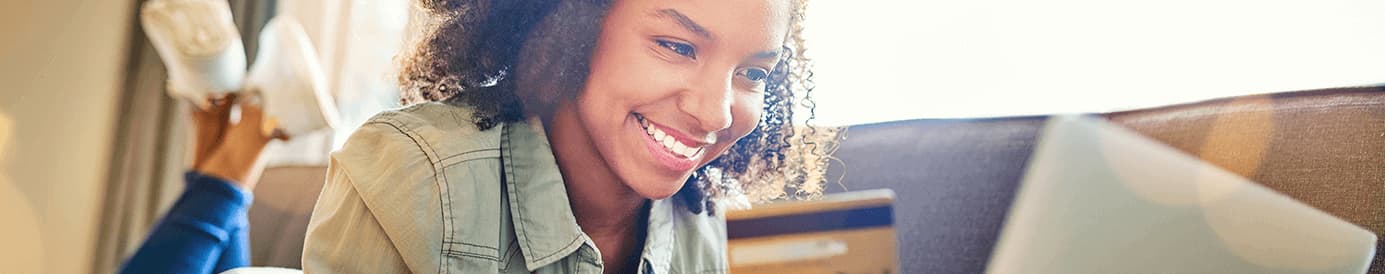 A woman holding a credit card while smiling at her laptop