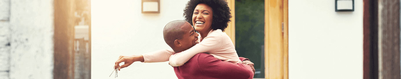 A man and a woman smile and hug in front of a door while the woman holds keys in her right hand