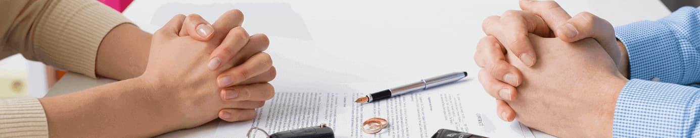 Two people have their hands clasped with two car key FOBs, two rings, a pen, and a sheet of paper in between them