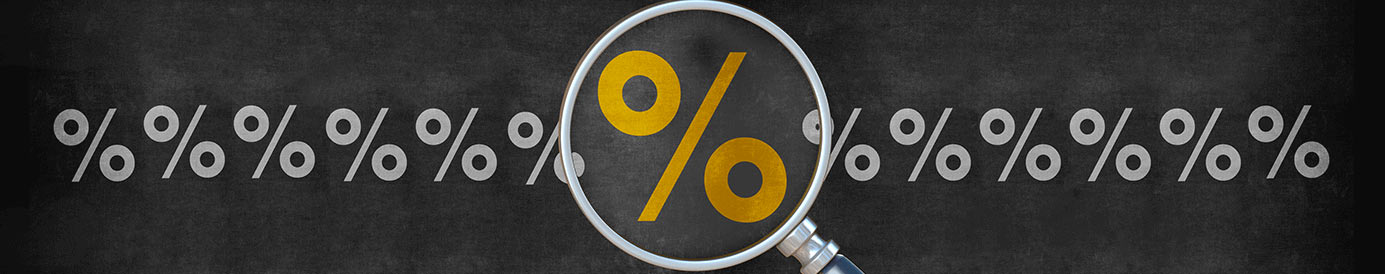 There is a row of grey percentage rate symbols on a chalkboard background. In the center, a magnifying glass is making one yellow percentage rate symbol look larger than the rest.