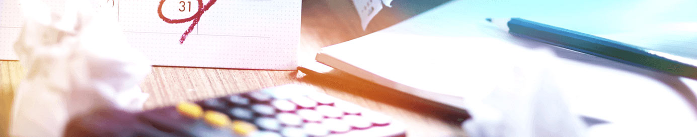 A calendar with the 31st circled in red with a notebook, a blue pencil, a calculator, and a crumpled ball of paper sit in the foreground