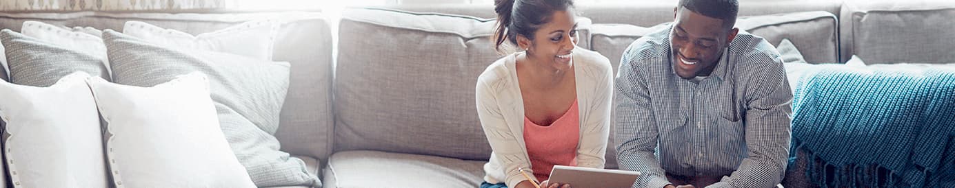 A woman and a man sitting next to each other on a couch smiling at a tablet