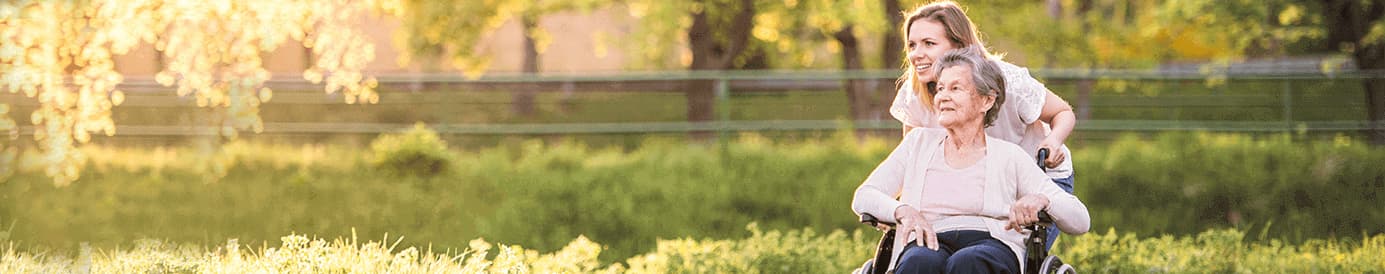 A smiling young woman pushing a smiling older woman in a wheelchair