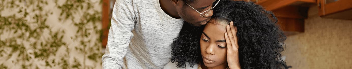 A man in glasses holds a woman who is holding her head with her left hand and seems overwhelmed