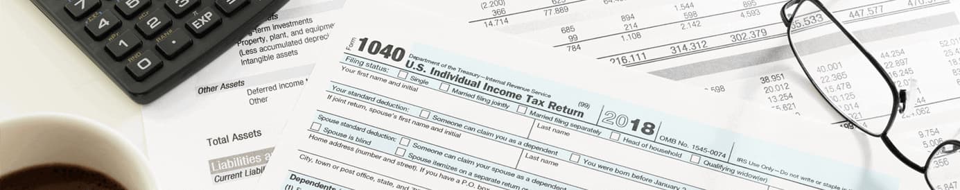 A US Individual Income Tax Return Form resting on other papers with a calculator, coffee mug, and glasses