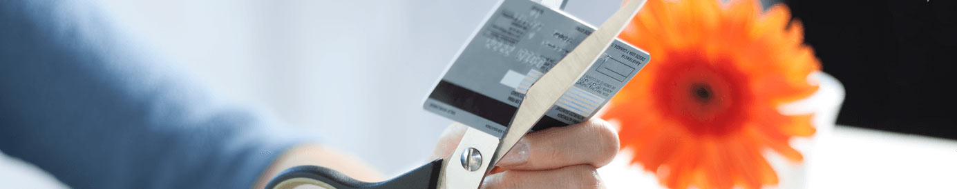 A person cutting their credit card using a pair of scissors with an orange flower in the background