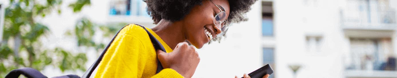 A woman wearing glasses looking at a cellphone she is holding in her left hand