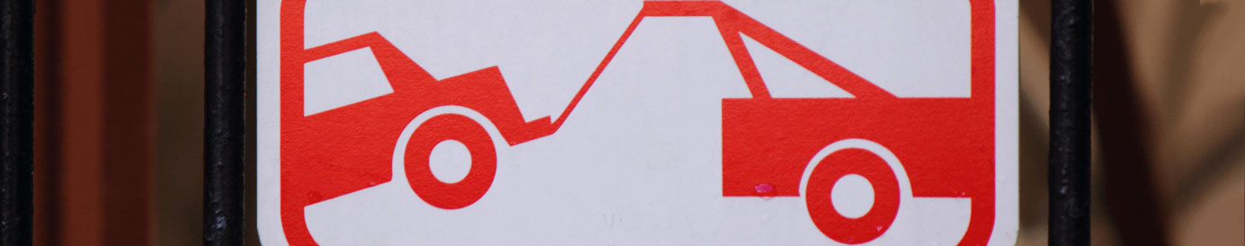 A red and white tow sign attached to an iron fence.