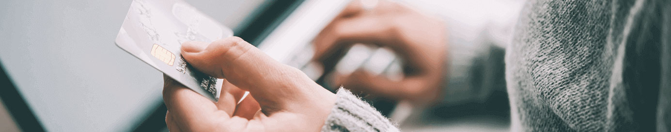 A person is holding a credit card in their hand while typing on a laptop.