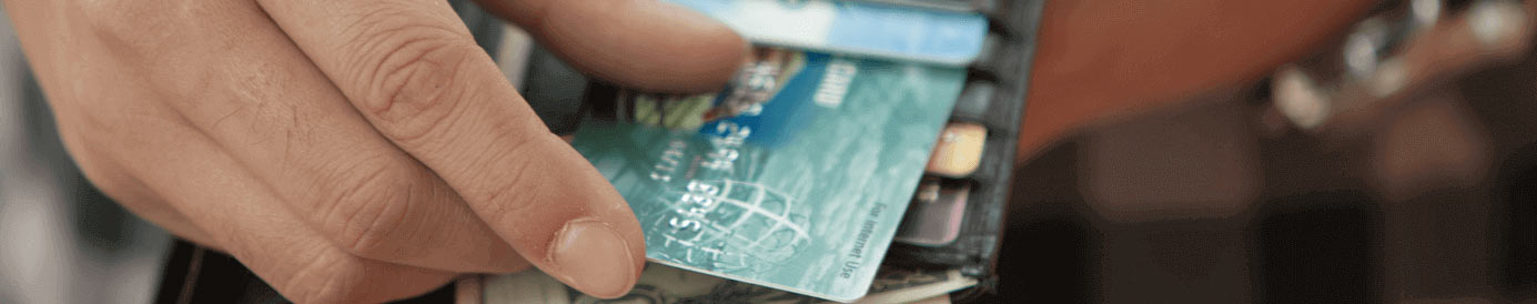 A person pulling a credit card out of a black leather wallet with other credit cards