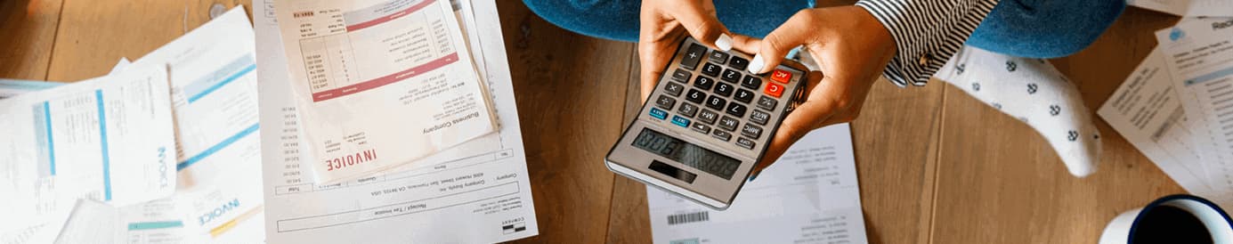 A woman holding and typing on a calculator with both hands sitting next to a man holding an invoice with his left hand