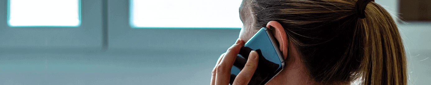 A woman with a ponytail holds a cellphone up to her left ear