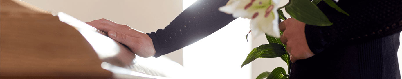 A person putting their right hand on a closed casket while the left hand holds a flower