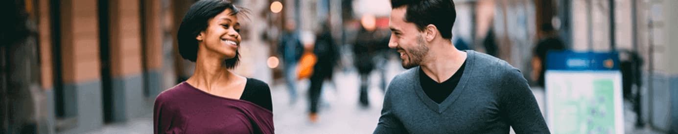 A woman and a man walking down the street while holding hands and smiling at each other