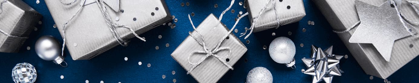 Silver boxes wrapped with silver twine sitting on a blue background with silver ornaments and glitter around them