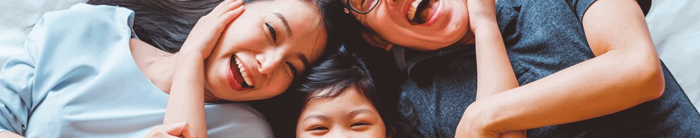 A smiling woman and a smiling man with glasses being hugged by a young child