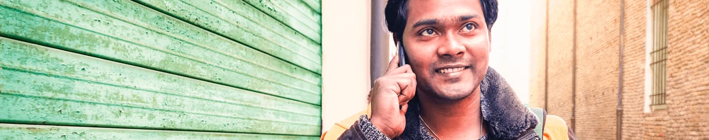 A man smiling while holding a cellphone to his right ear